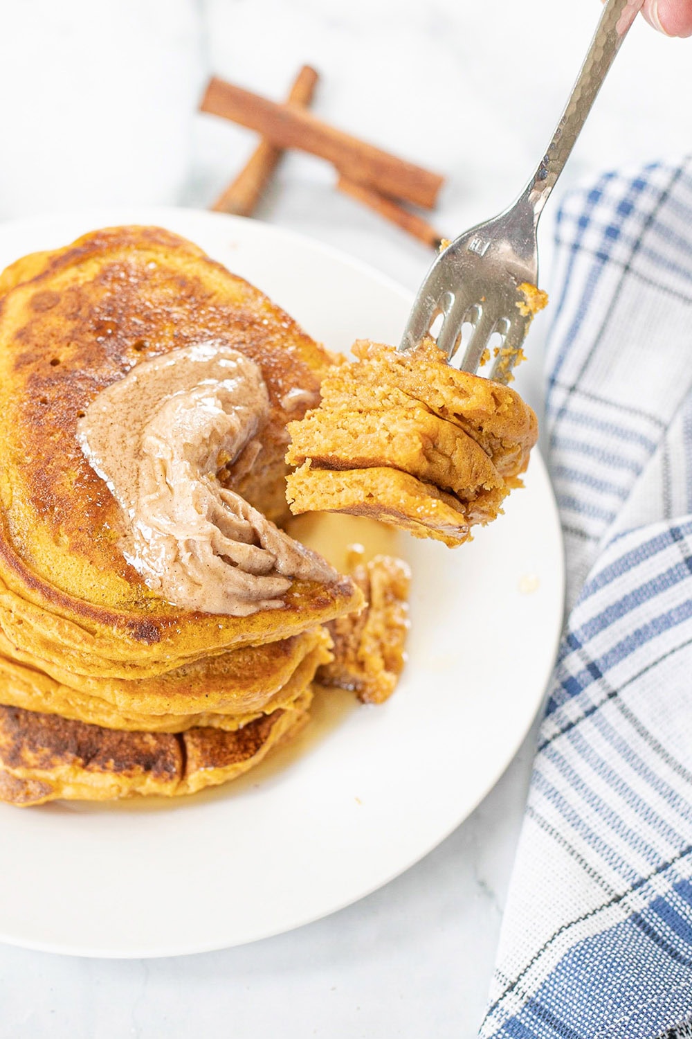 Fork full of pancakes above the plate of pumpkin pancakes.