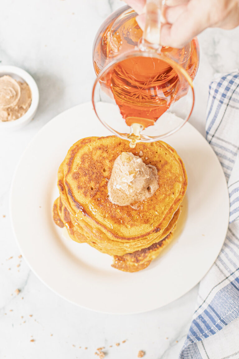 Pouring syrup over pumpkin pancakes with a scoop of cinnamon butter.