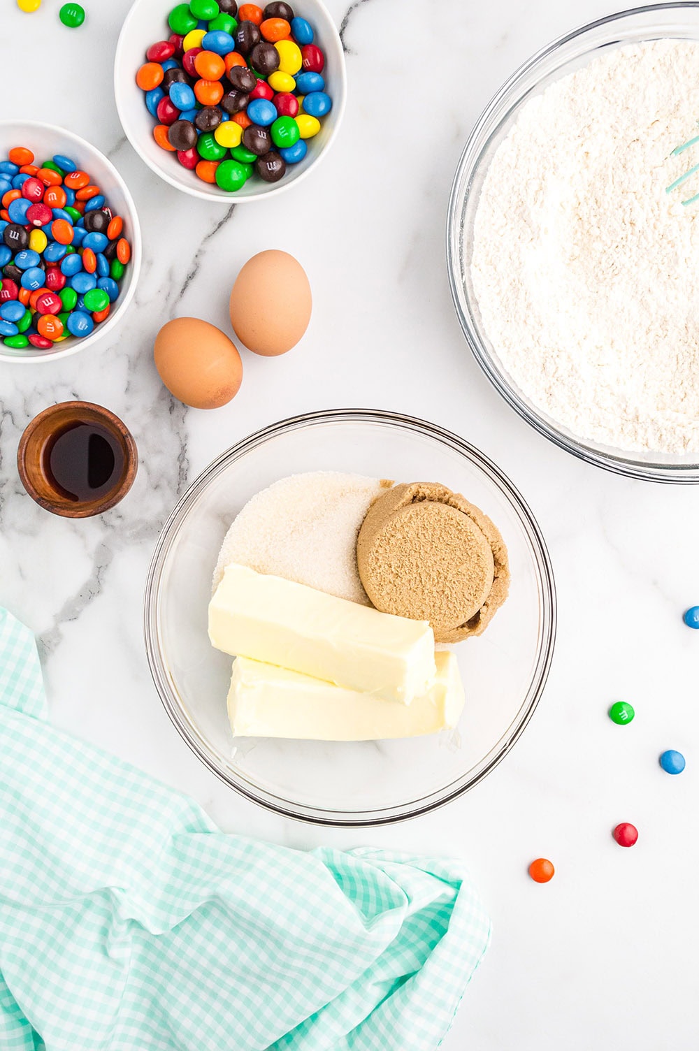 Butter and brown sugar in a bowl along with other cookie ingredients on a table.