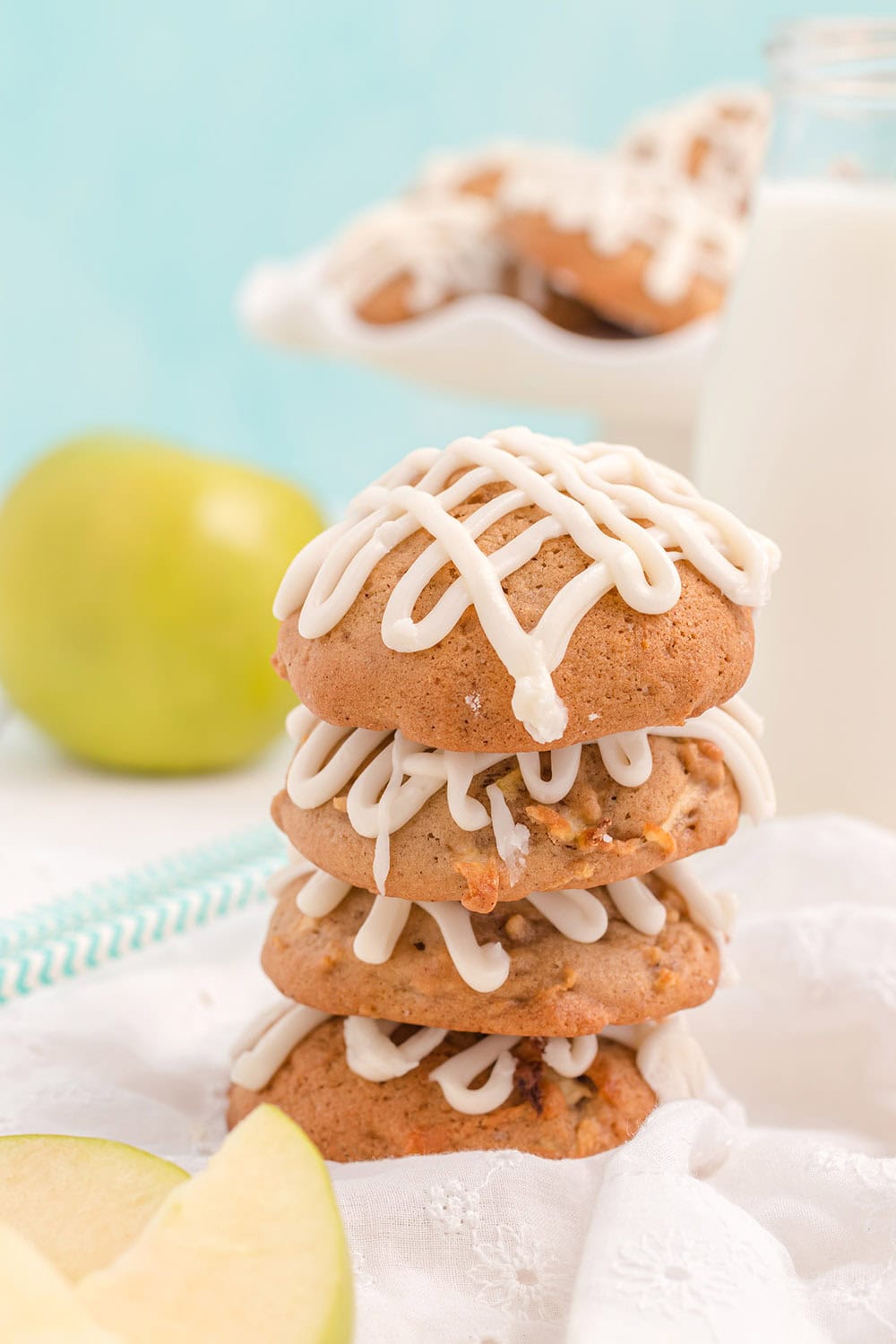 Stacked apple cookies with glaze and an apple in the background.