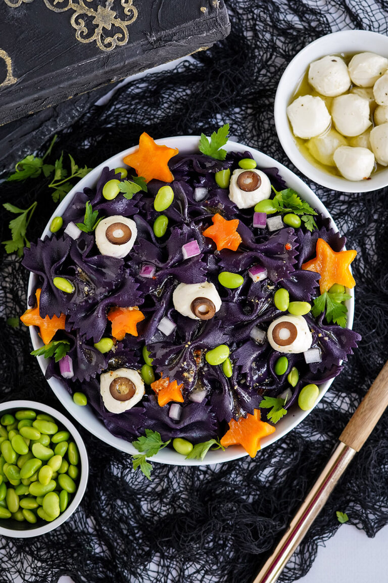 Bowl of bat pasta salad on a table surrounded by ingredients.
