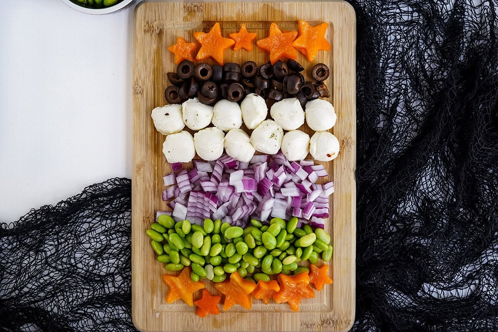 Rows of chopped ingredients for pasta salad on a cutting board.
