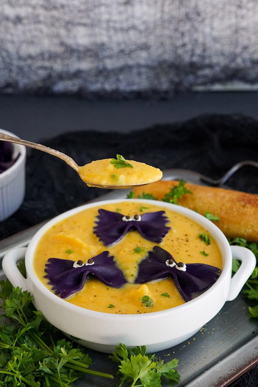 Raised spoon with butternut squash soup with bowl in the background.