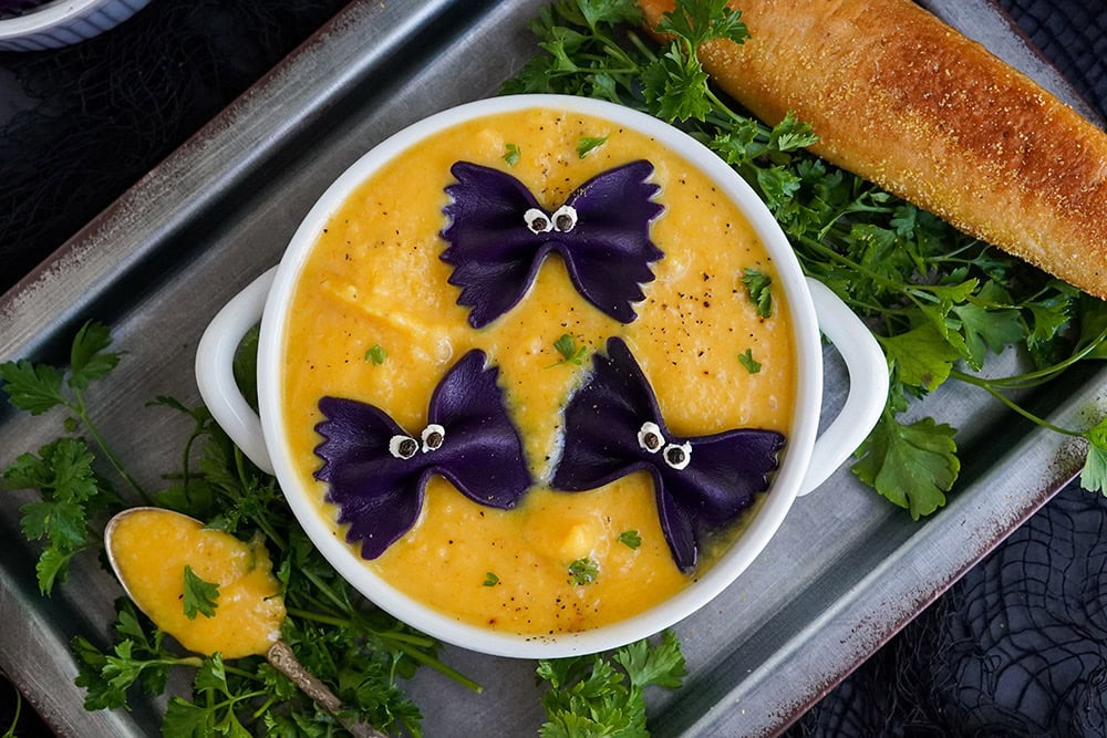 Bowl of soup on top of a pan. Black pasta tops the butternut squash soup.