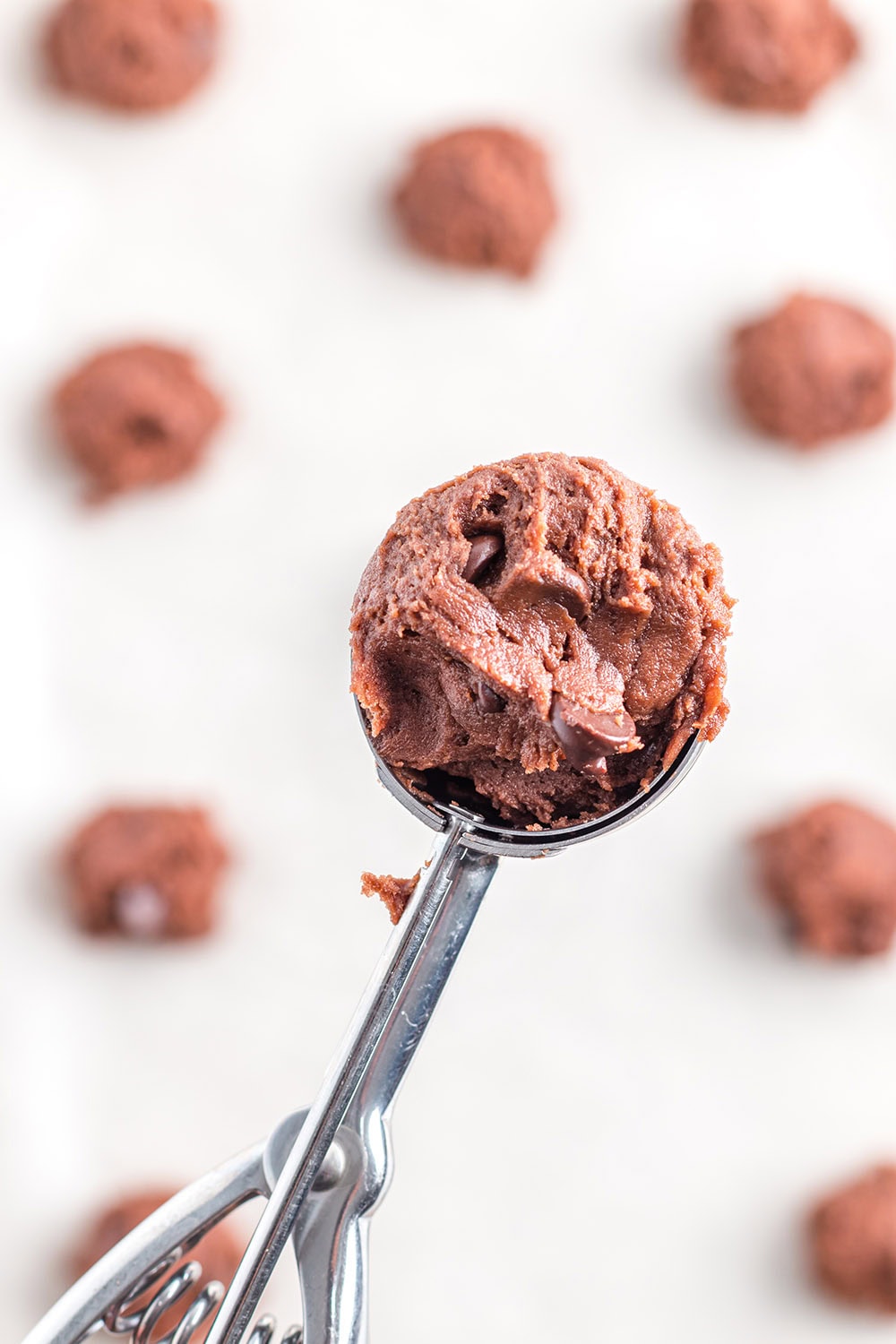 Cookie dough in a scoop above a baking sheet. 