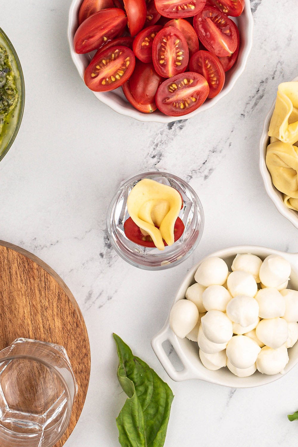 Pasta and tomatoes in a jar with bowls of cheese and tomatoes on the table. 