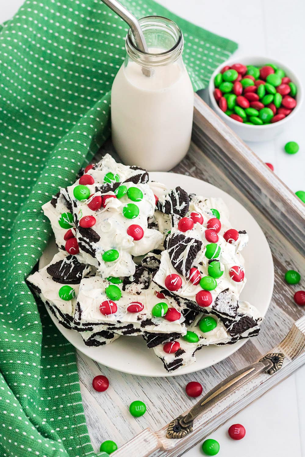 Overhead image of a plate of bark candy next to milk and holiday M&Ms.