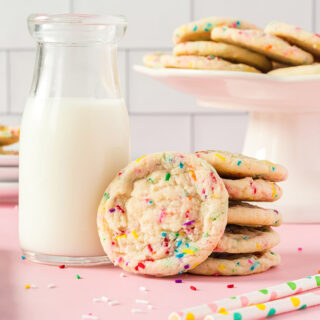 Funfetti cookies on a stand, stacked in front of the stand, and next to a glass of milk.