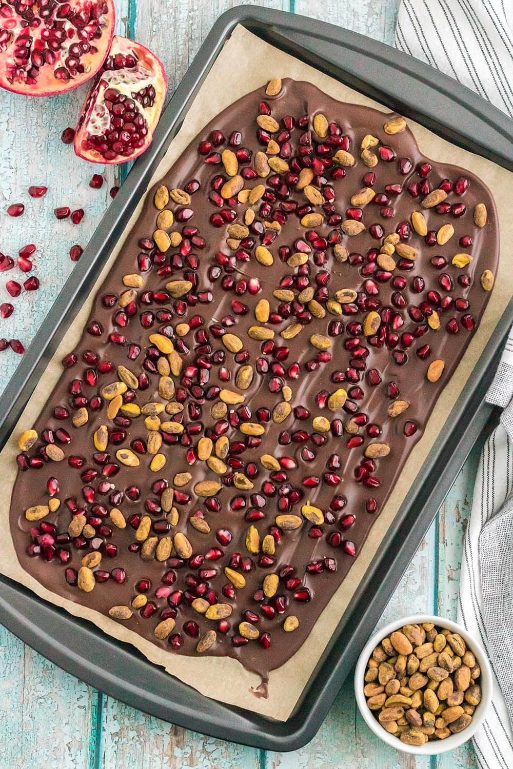 Chocolate bark in a baking sheet topped with pomegranate arils and pistachio nuts.