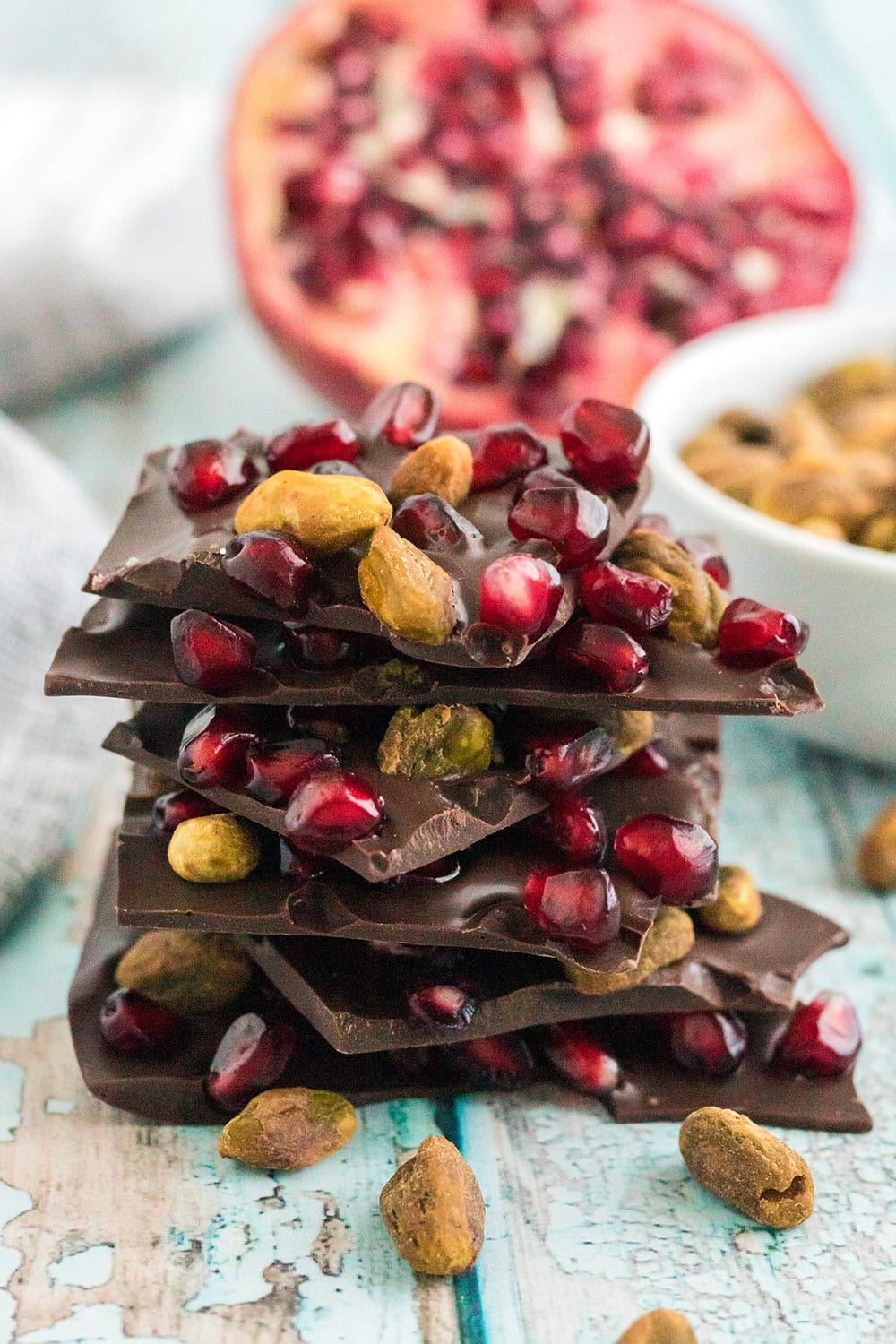 Chocolate pistachio bark pieces stacked with pomegranate in the background.