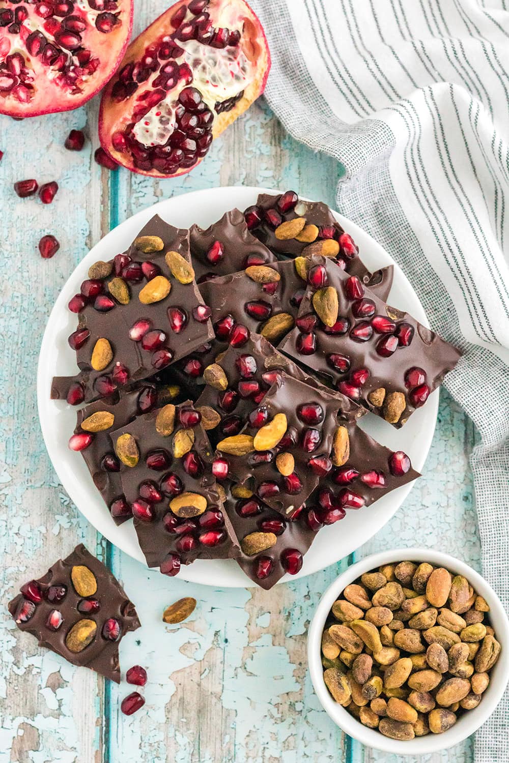 Bark candy on a plate next to pistachios and pomegranates.