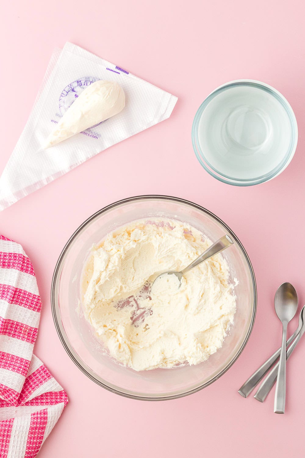 Icing in a bowl next to a piping bag and spoons. 
