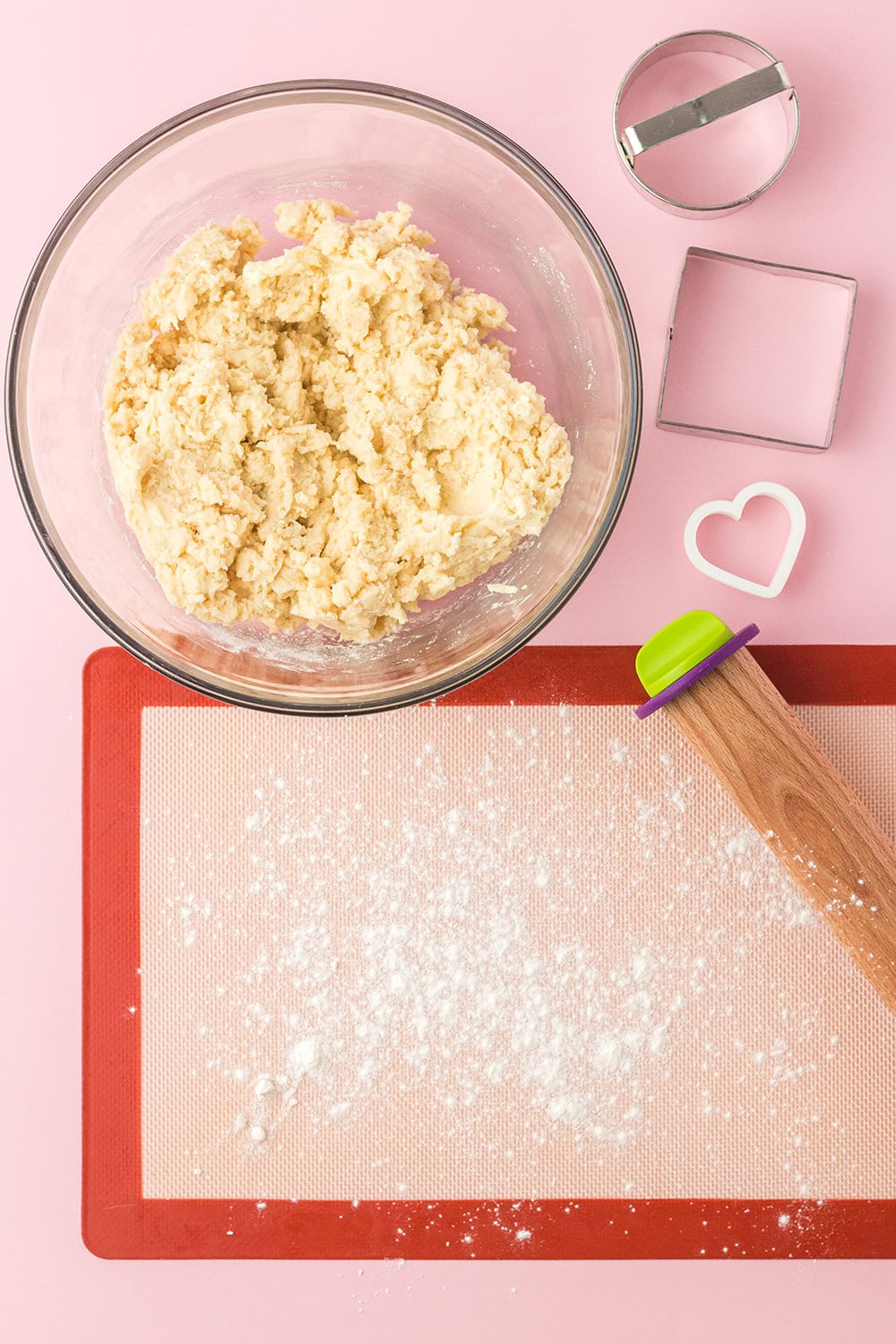 Cookie dough next to a rolling pin, cookie cutters, and flour coated surface. 