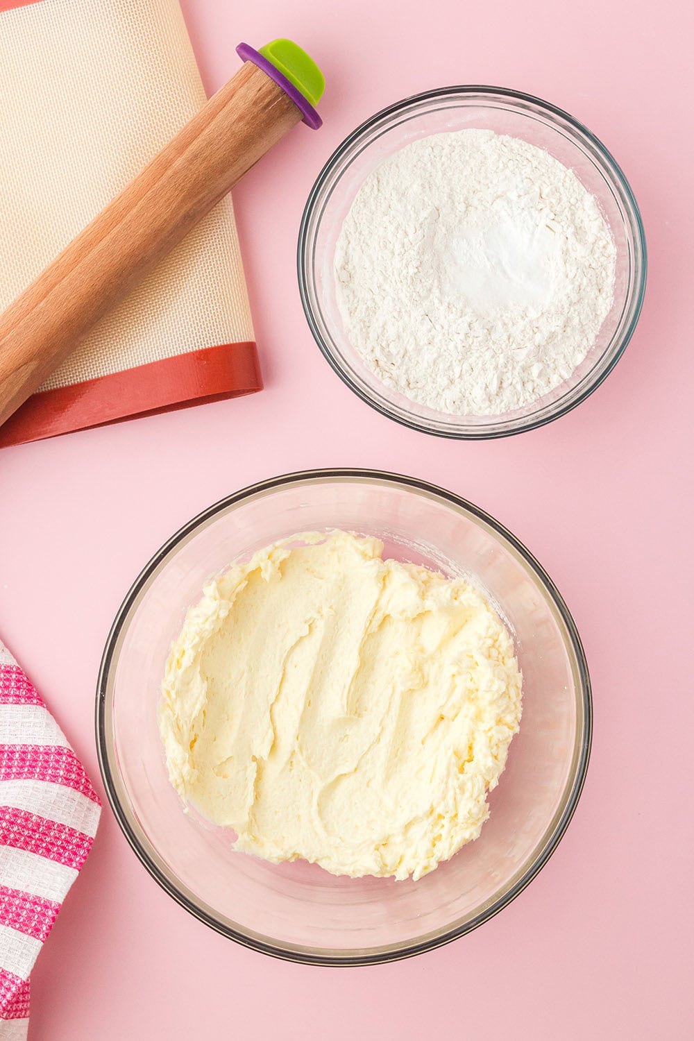 Wet and dry ingredients in two bowls next to a rolling pin. 