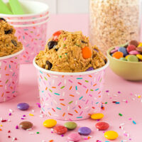 Cups of monster cookie dough next to M&M candies and oats.