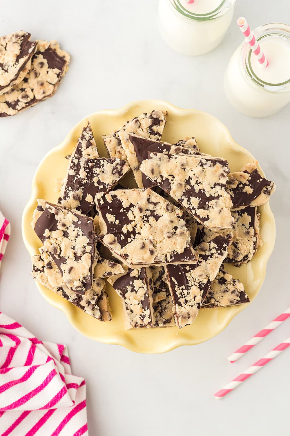 A yellow plate with cookie dough bark candy next to milk.