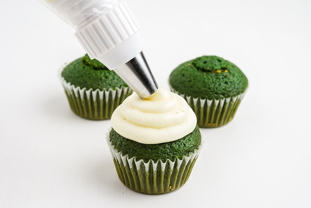Piping white frosting onto green cupcakes.