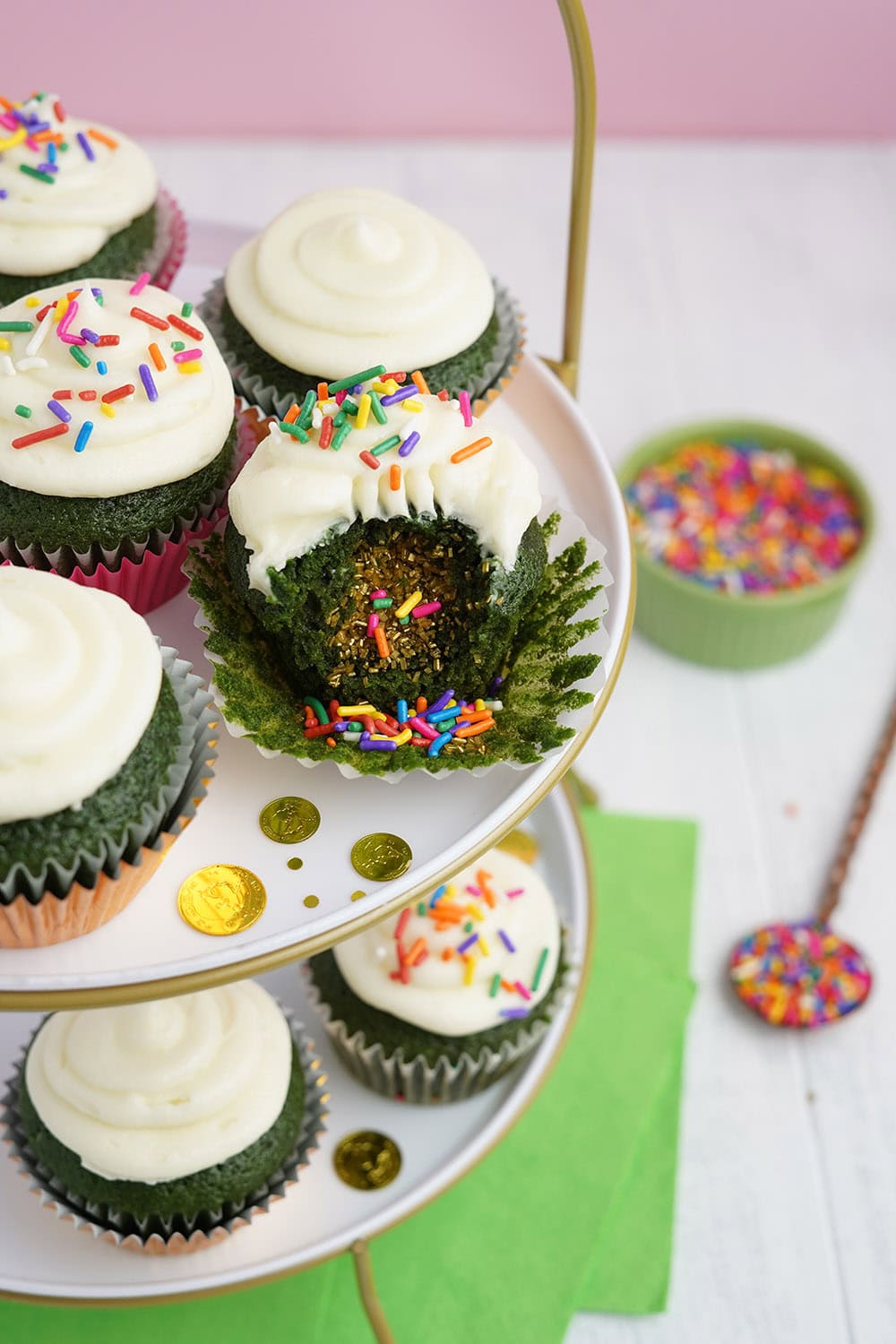 Cupcakes on a tray. One of them has a bite taking out showing the surprise filling of sprinkles. 