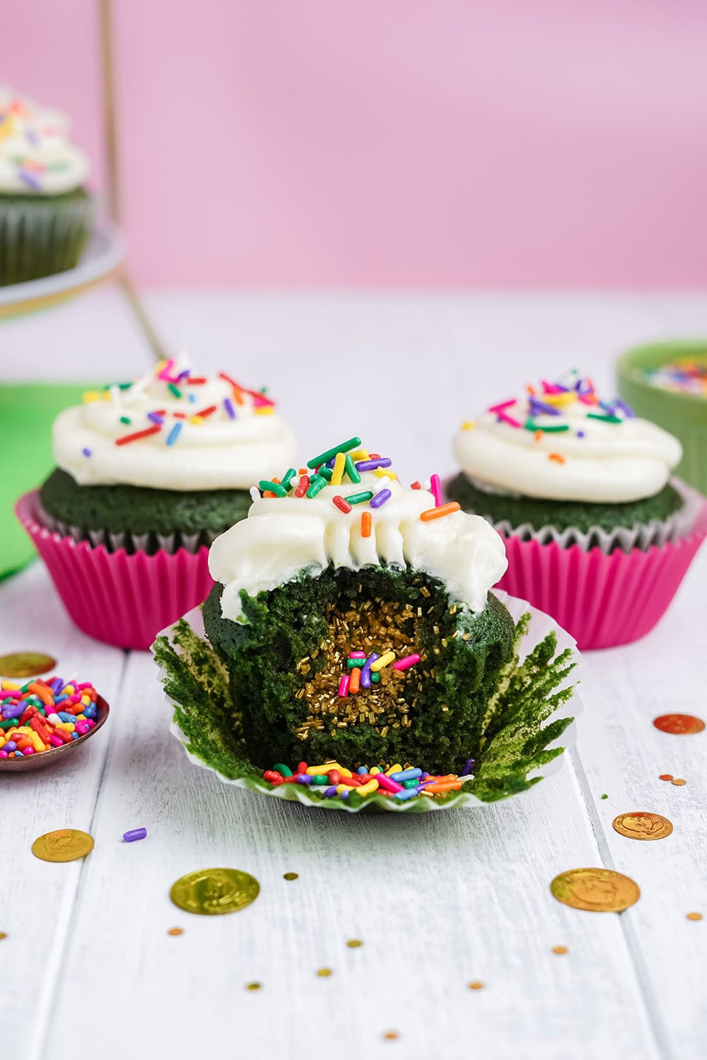 Three cupcakes with one unwrapped and gold sprinkles as filling falling out. 