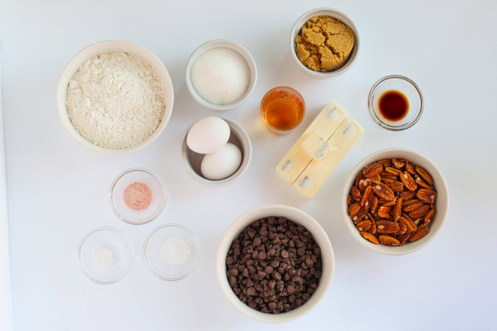 Flour, eggs, butter, pecans, chocolate chips, and other ingredients in bowls.