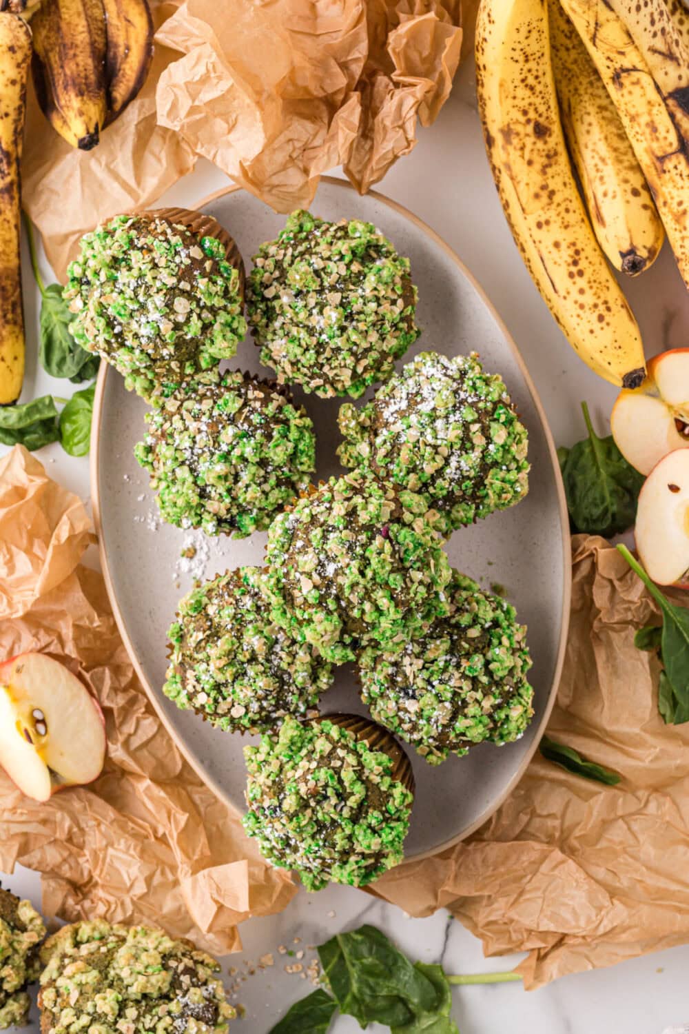 Tray of banana spinach muffins with a green topping next to bananas. 