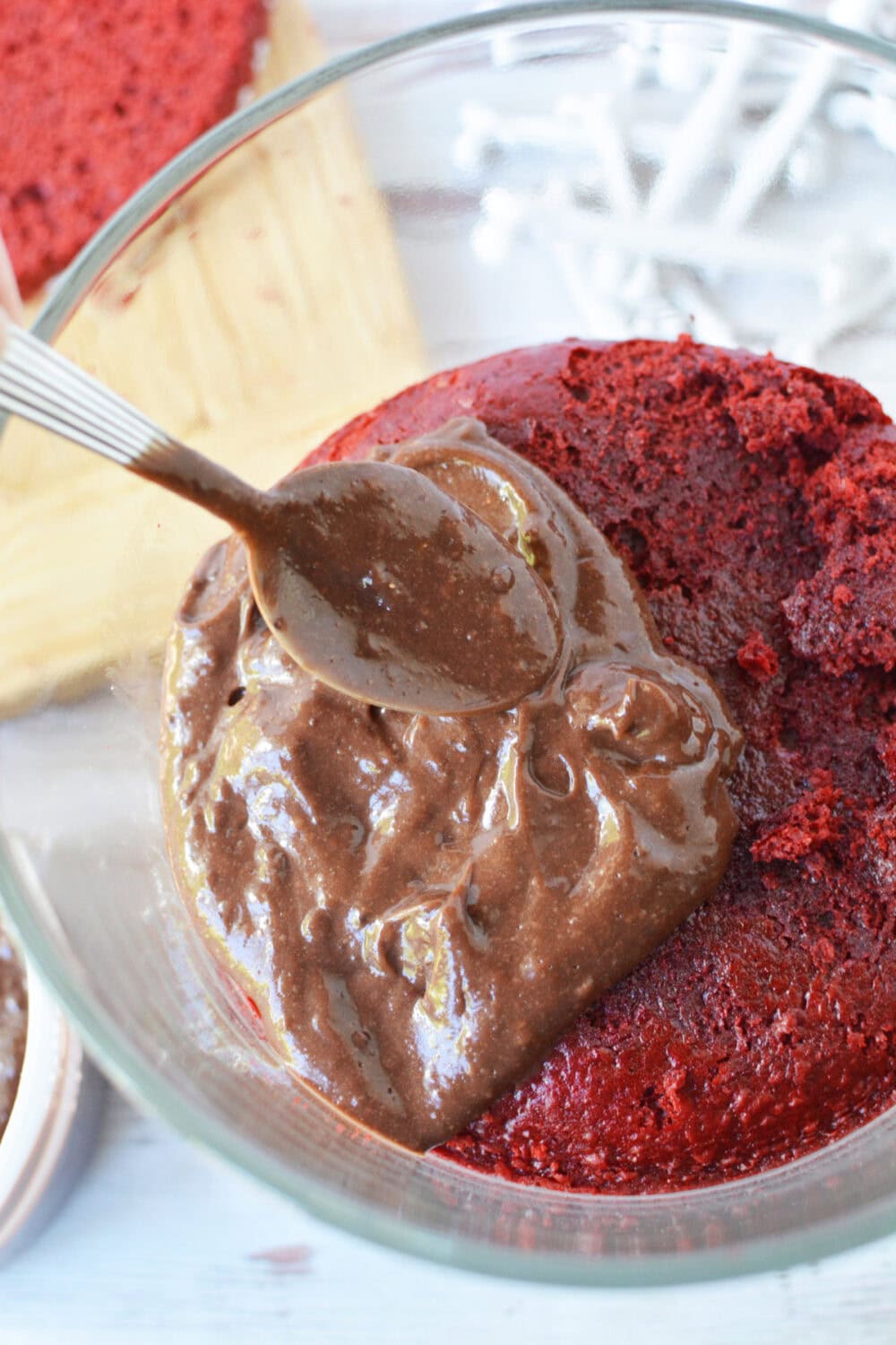 Putting chocolate pudding on top of a red velvet cake round in a trifle bowl. 