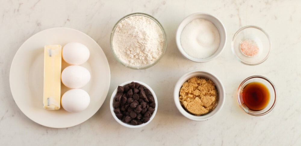 Butter, eggs, flour, chocolate chips, brown sugar, and vanilla in bowls. 