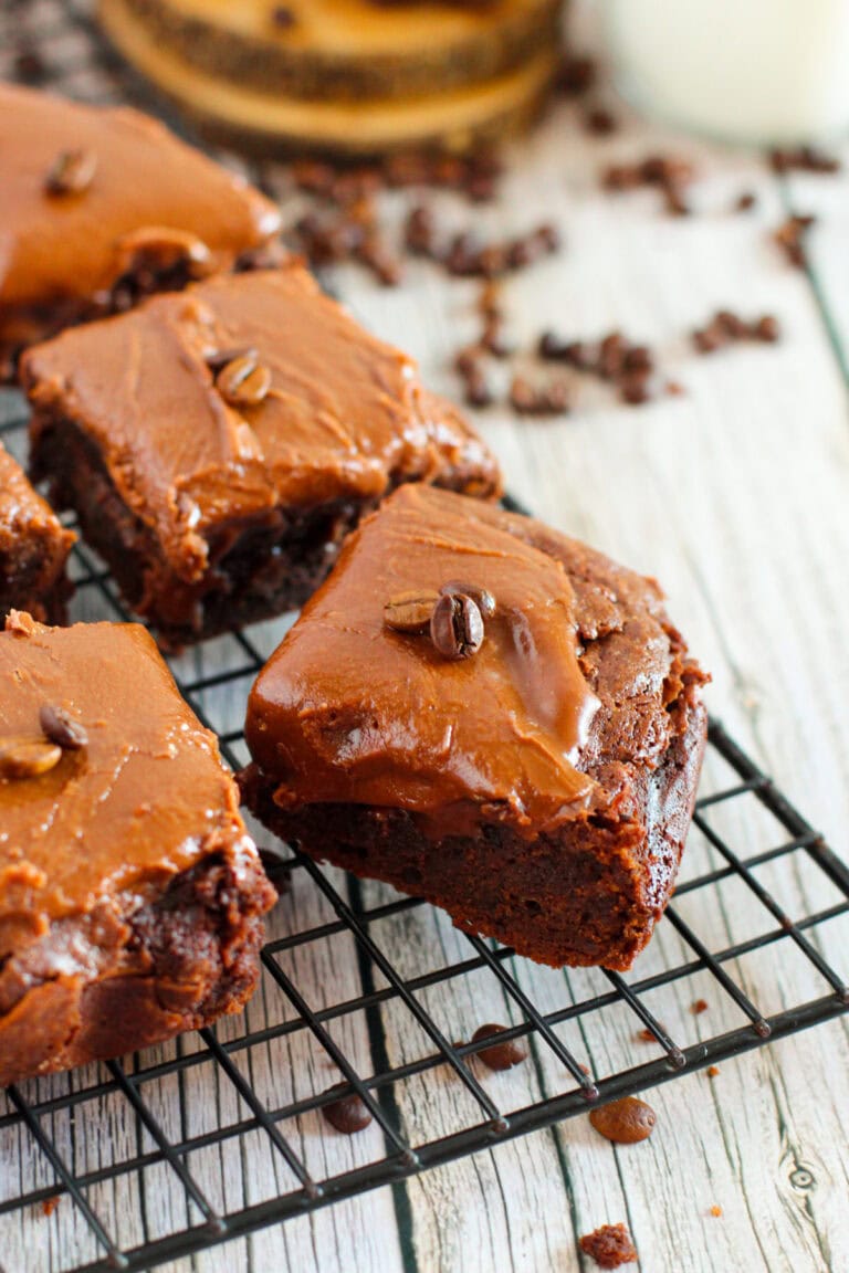 Brownies with frosting and coffee beans on a rack.