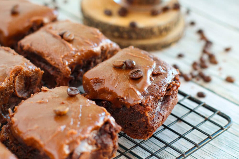 Chocolate frosted brownies on a rack with coffee beans on the table. 