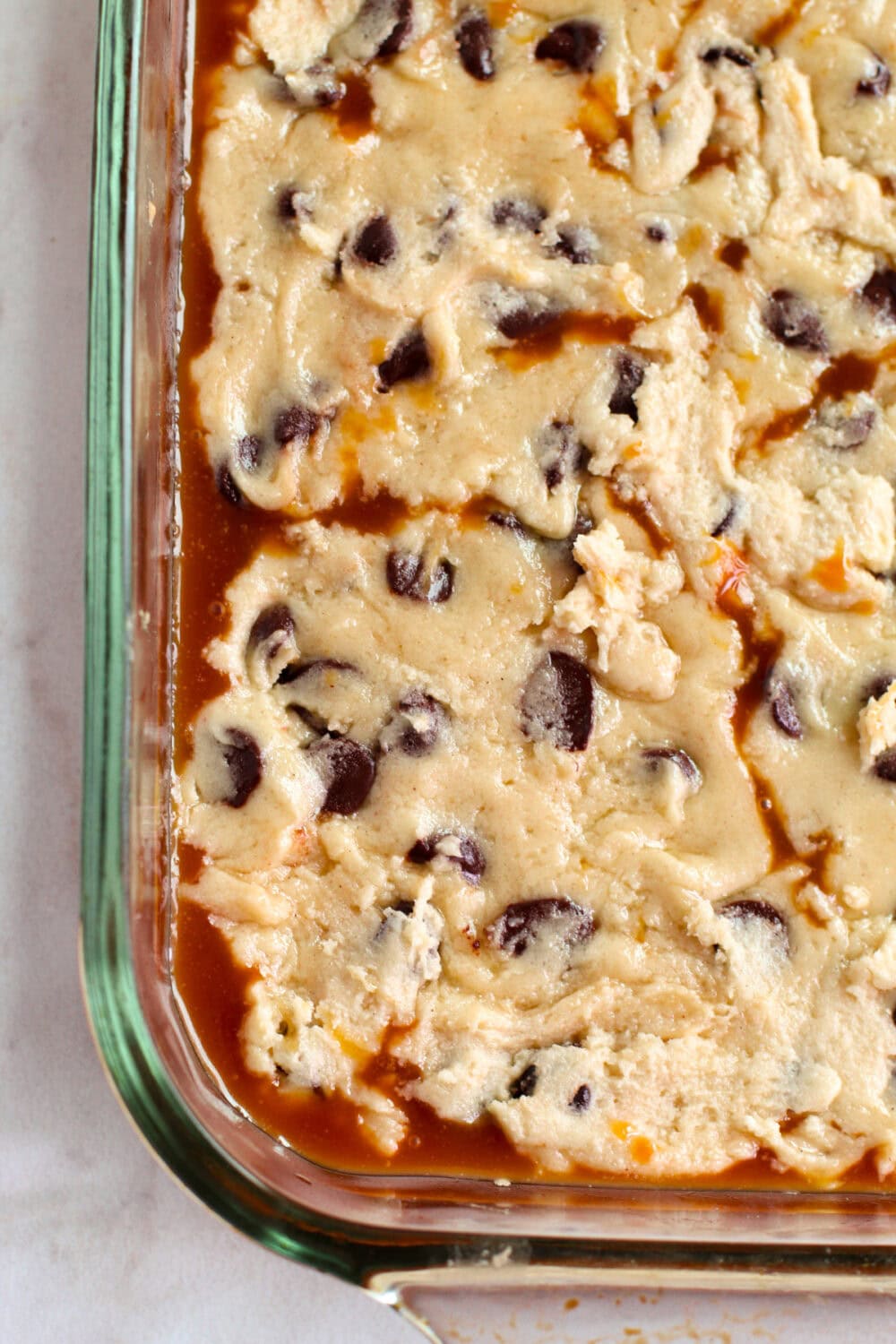 Cookie dough on top of a layer of caramel in a baking dish. 