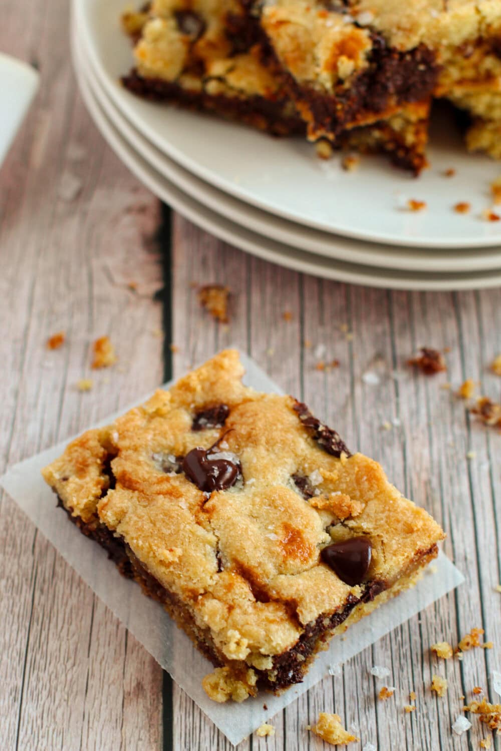 Slice of chocolate chip caramel cookie bar on a table next to the plate of them. 