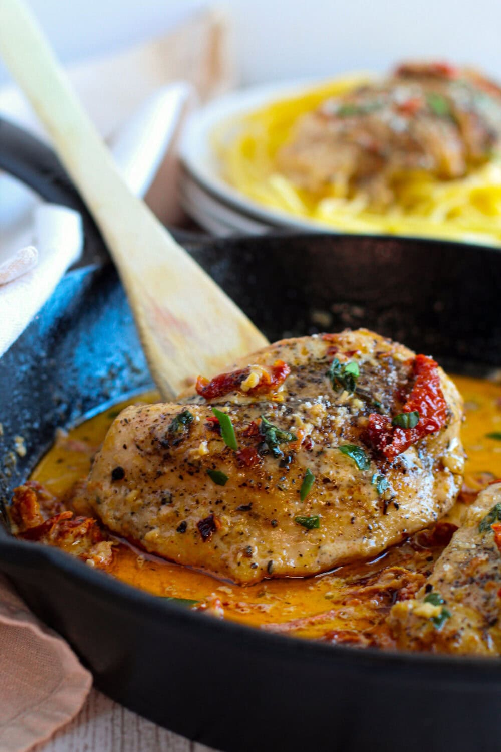 Marry me chicken in a skillet with pasta in the background.