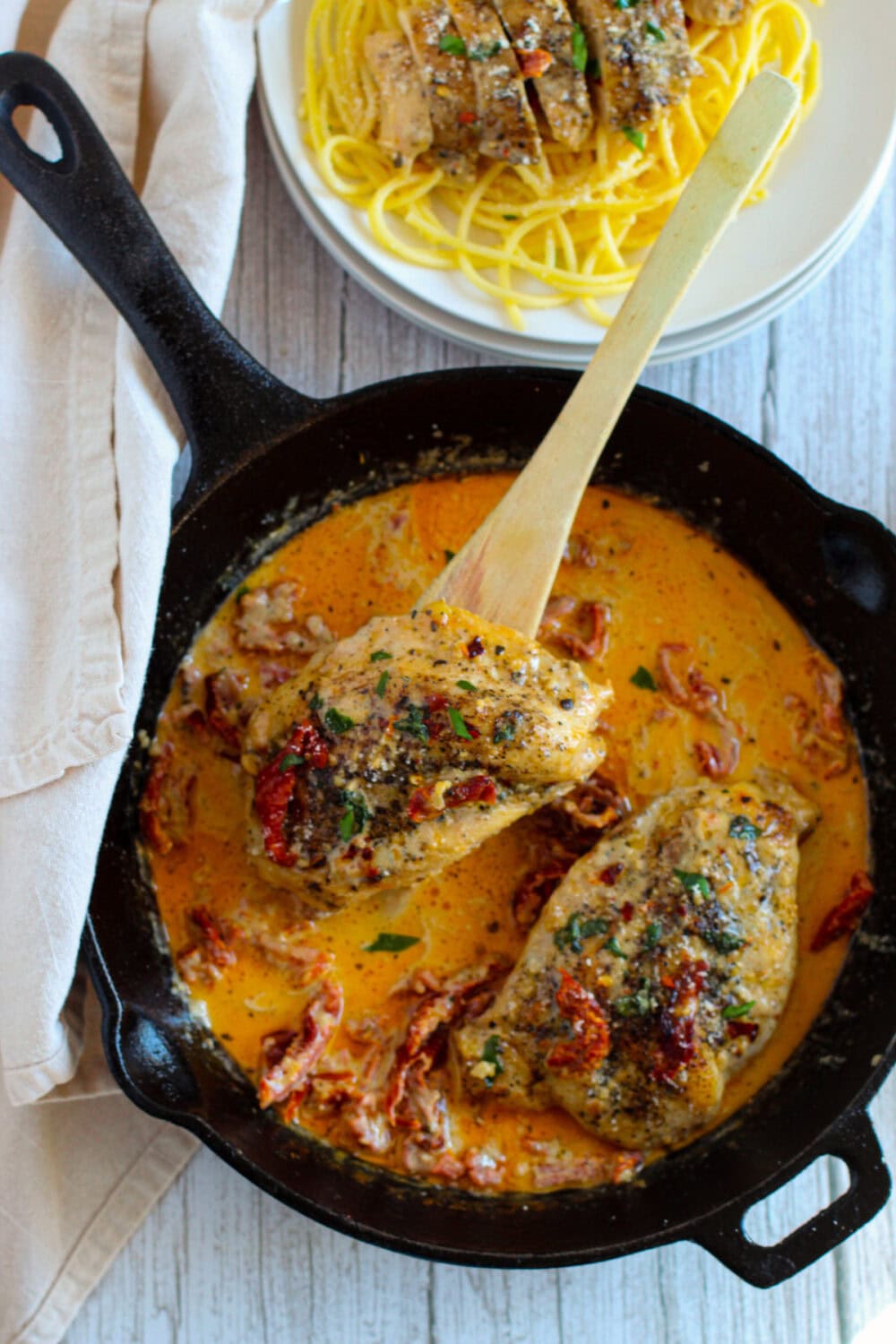 Skillet with a wooden spoon lifting out a piece of Marry Me Chicken.