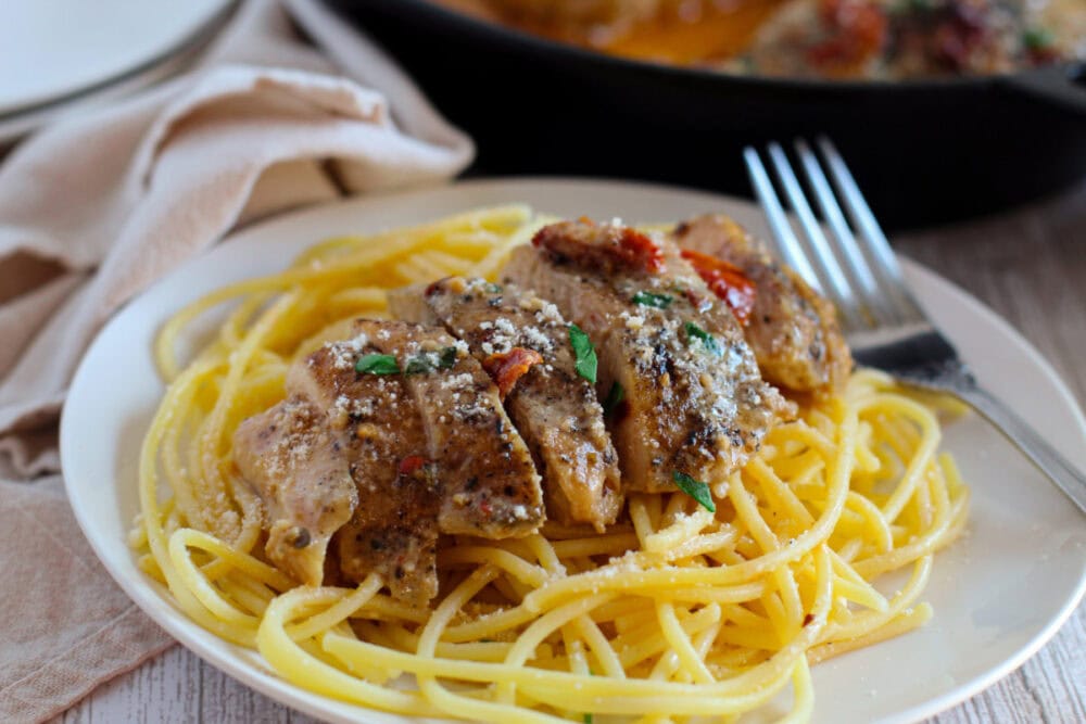 Marry Me chicken sliced on top of pasta on a plate.