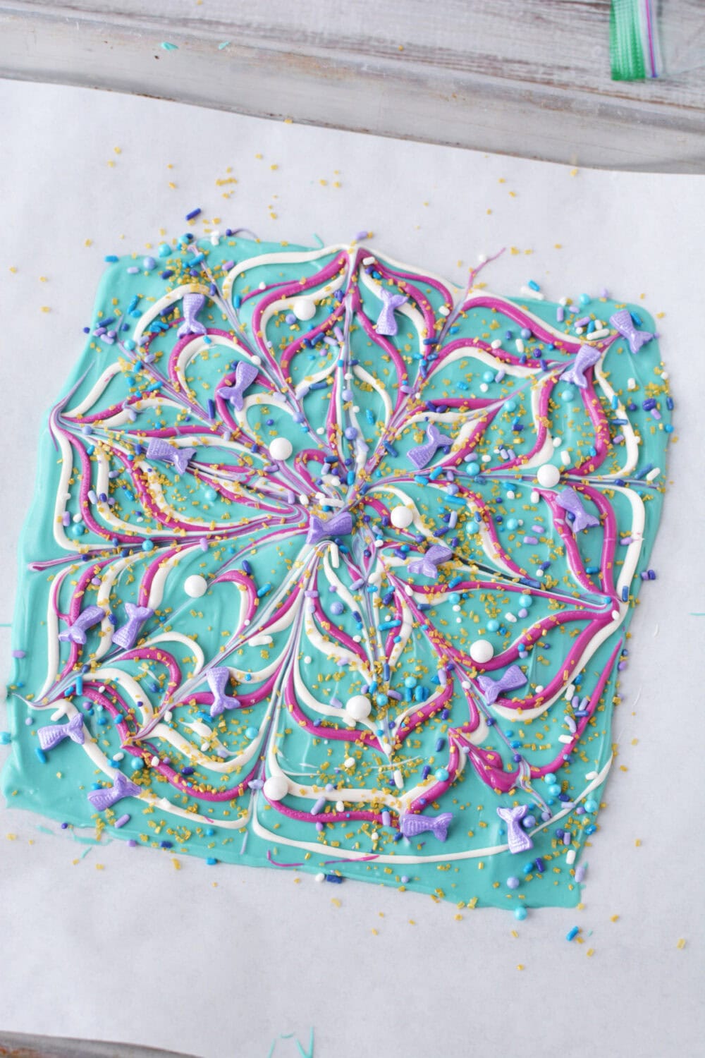 Swirls of candy melts and sprinkles on parchment paper on a sheet. 