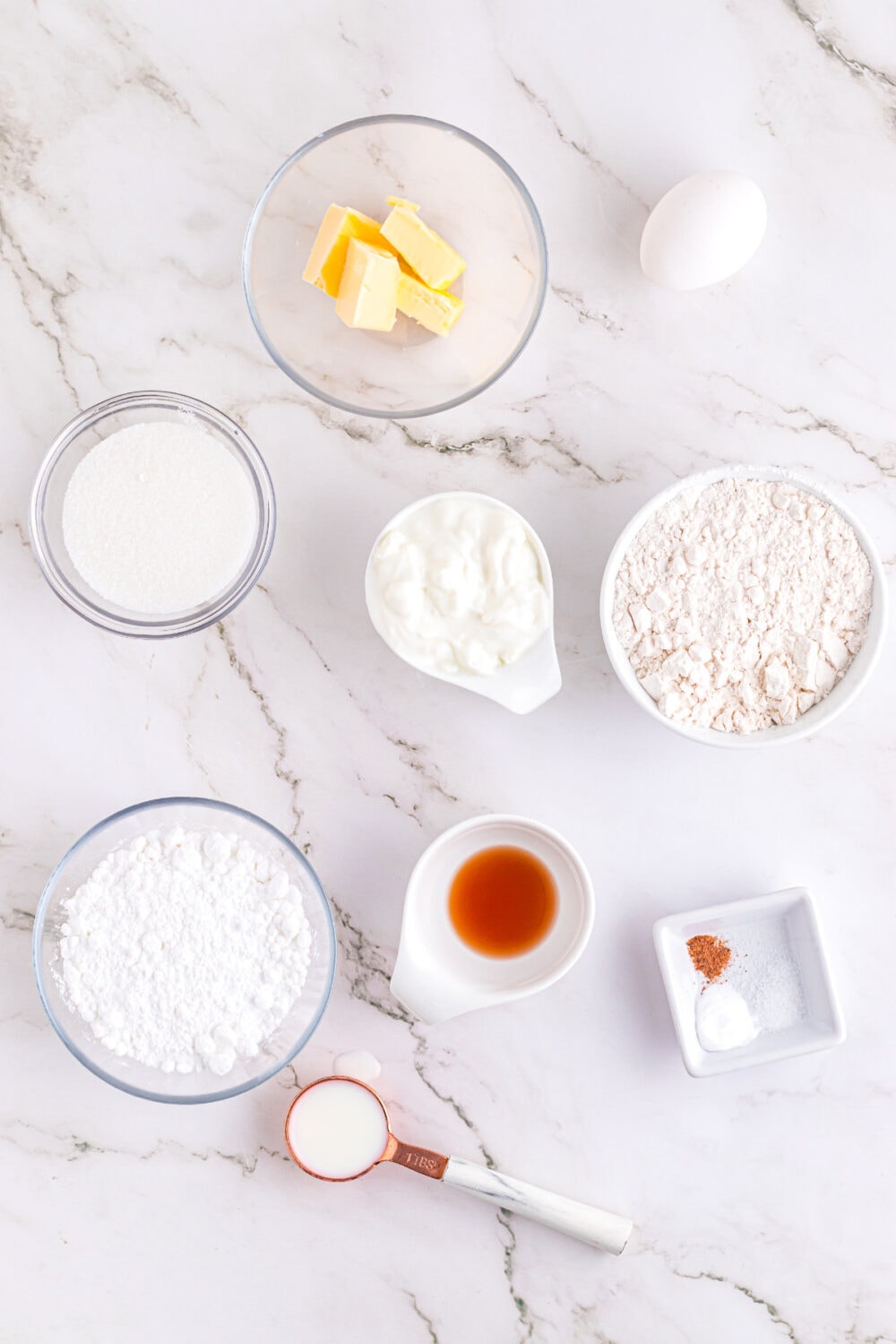 Butter, vanilla, milk, flour, sugar and other ingredients in bowls. 