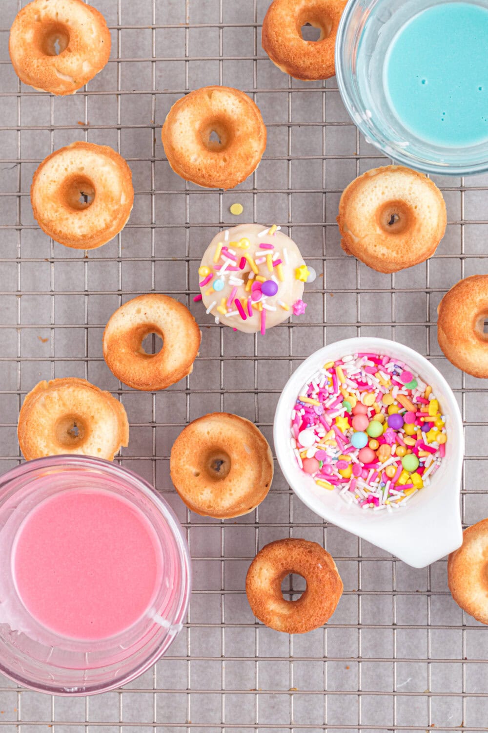 Baked donuts on a rack being decorated with sprinkles. 
