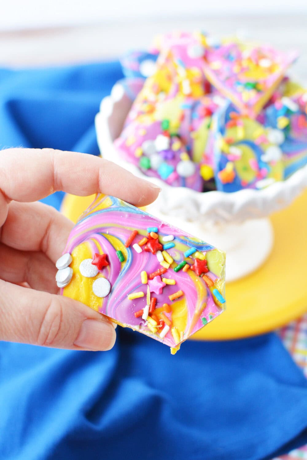 Holding a piece of rainbow chocolate bark candy. 