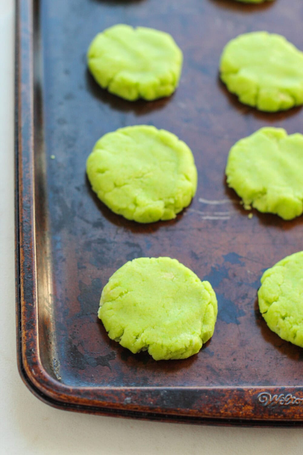 Flattened green cookie dough on a baking sheet.