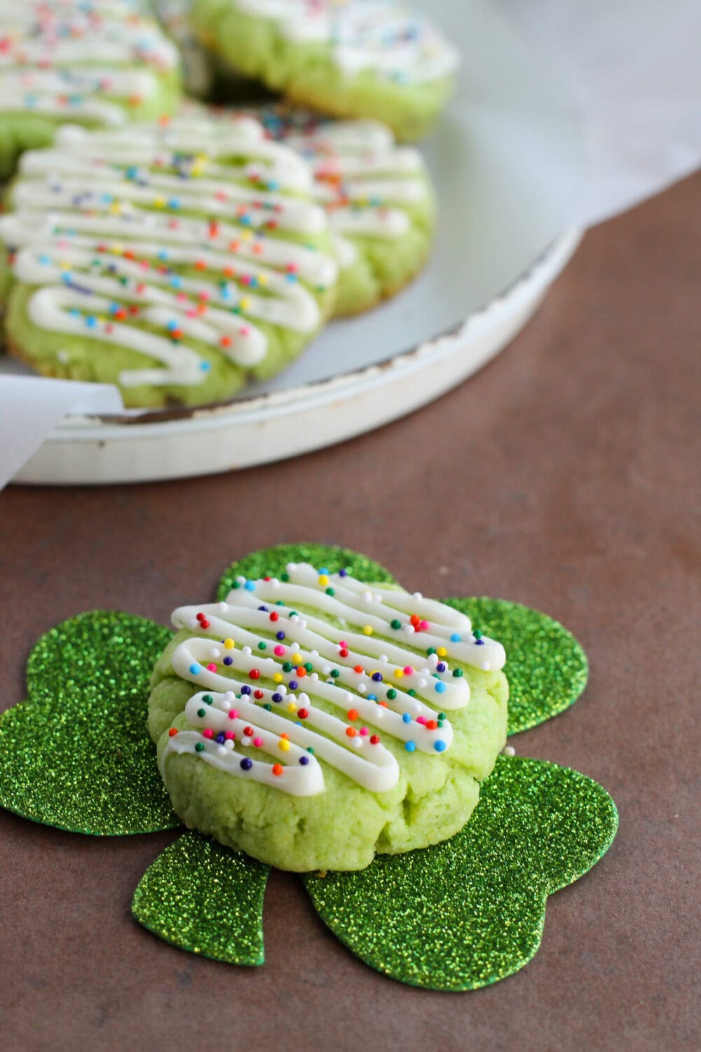 Green cookies with sprinkles. One sitting on a shamrock decoration.