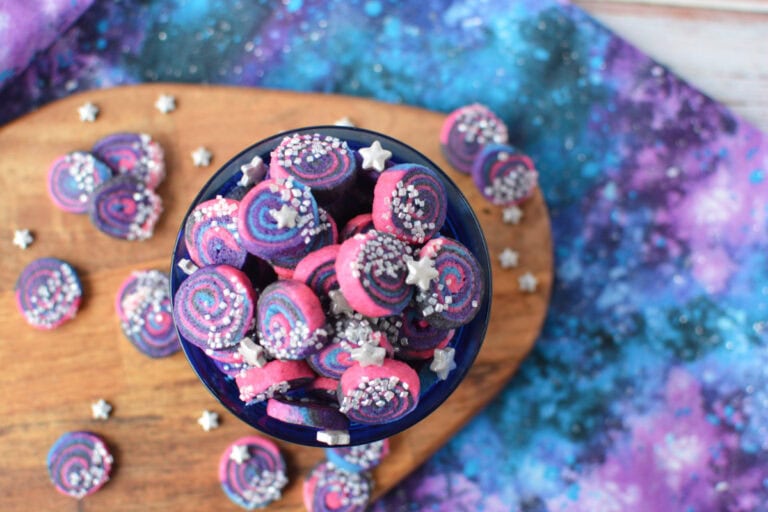 Galaxy shortbread bites in a cup with some on the table.