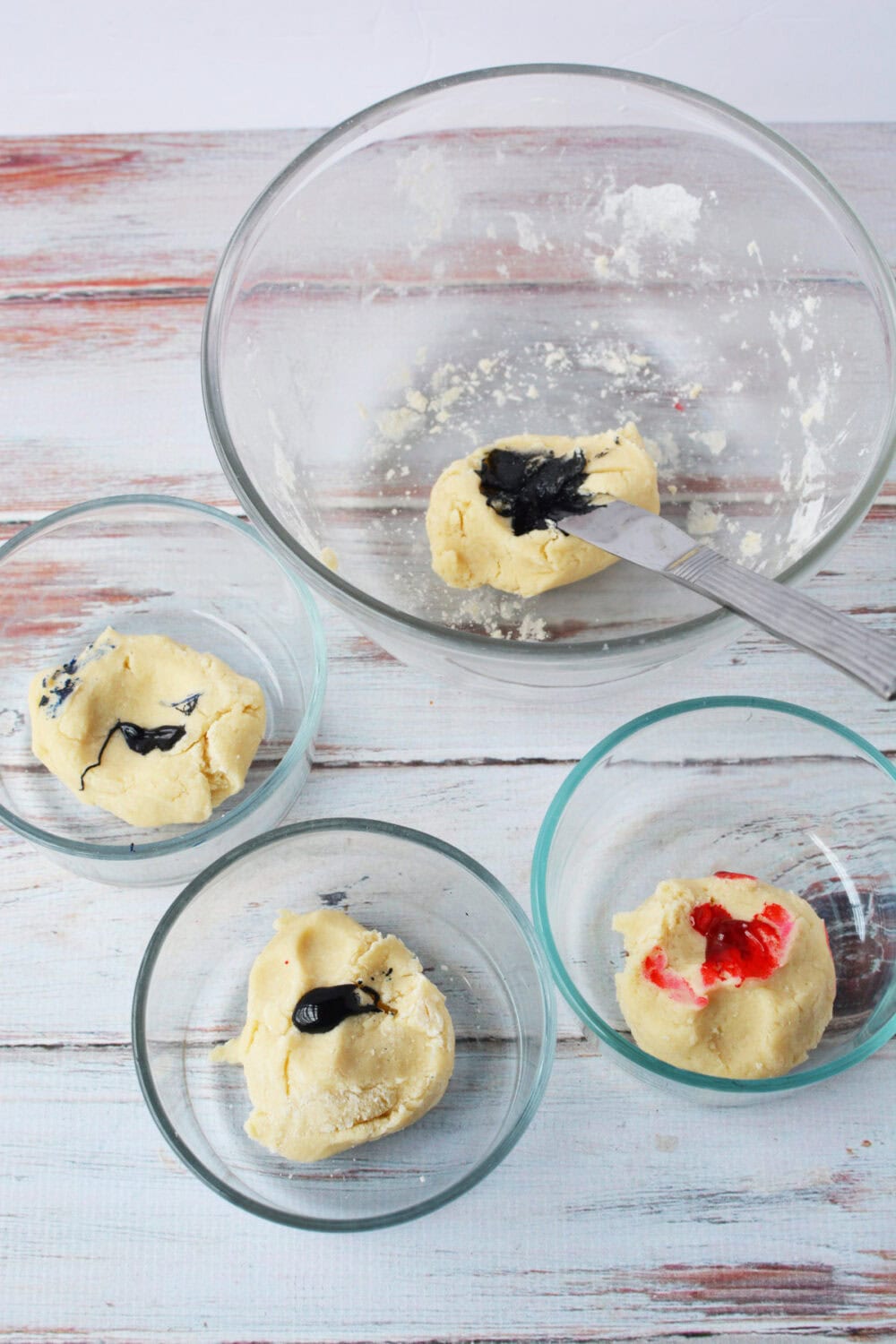 Four bowls of dough with drops of food coloring. 