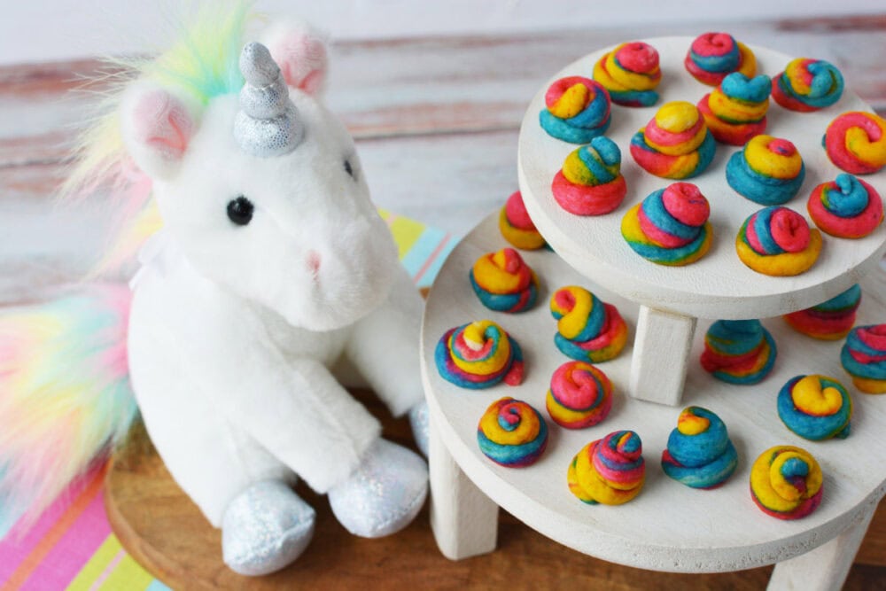 Plush unicorn sitting next to tiers of unicorn poop mini shortbread bites. 