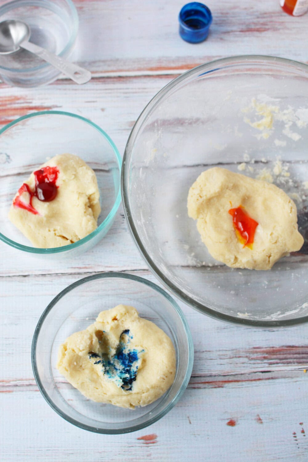 Dough with drops of food coloring in bowls. 