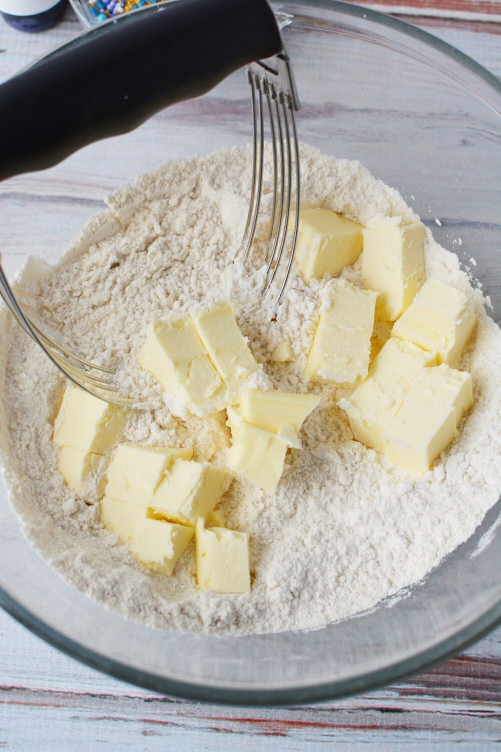 Chunks of butter in a bowl with a pastry blender.