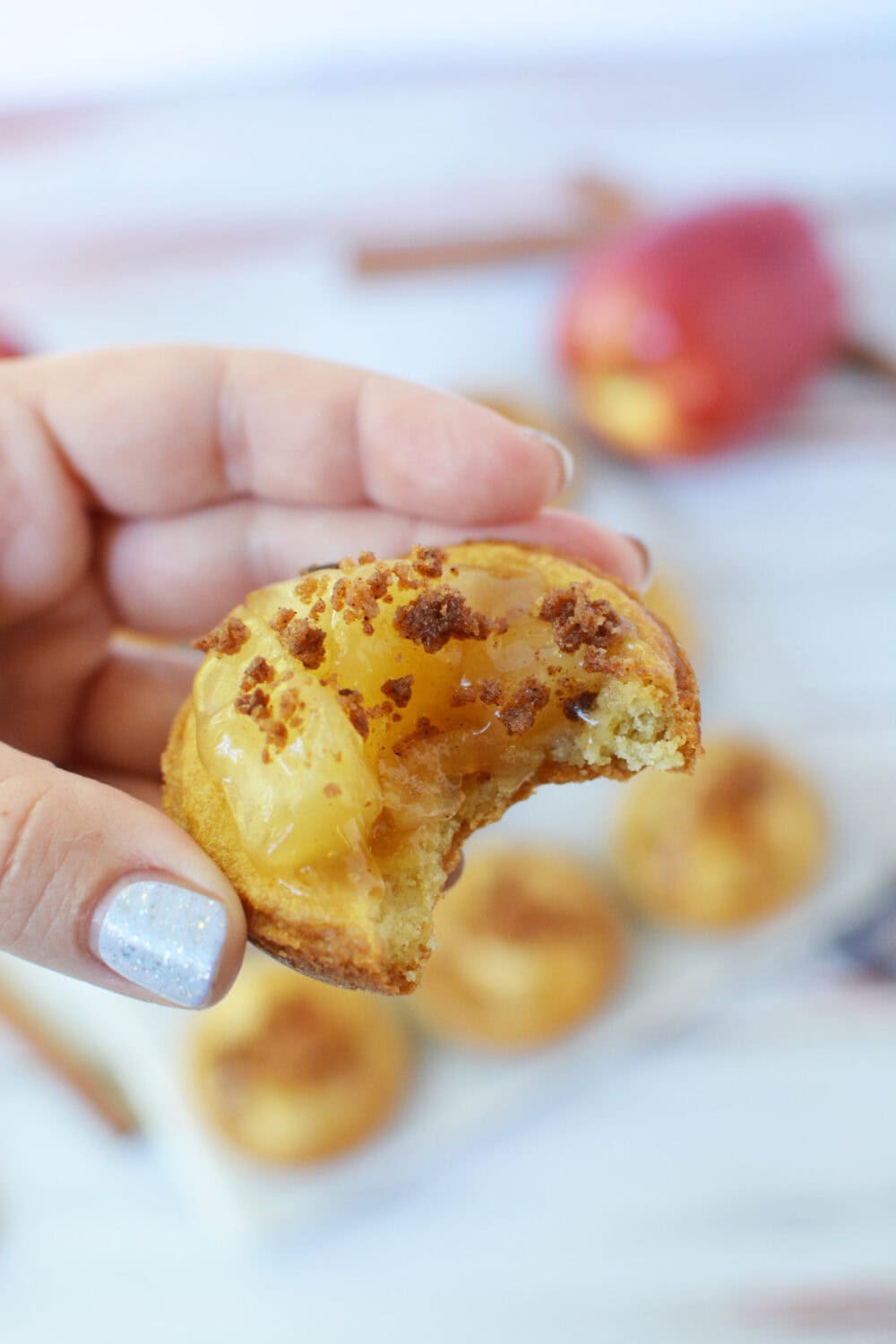 Holding an apple pie cookie with a bite taken out of it.