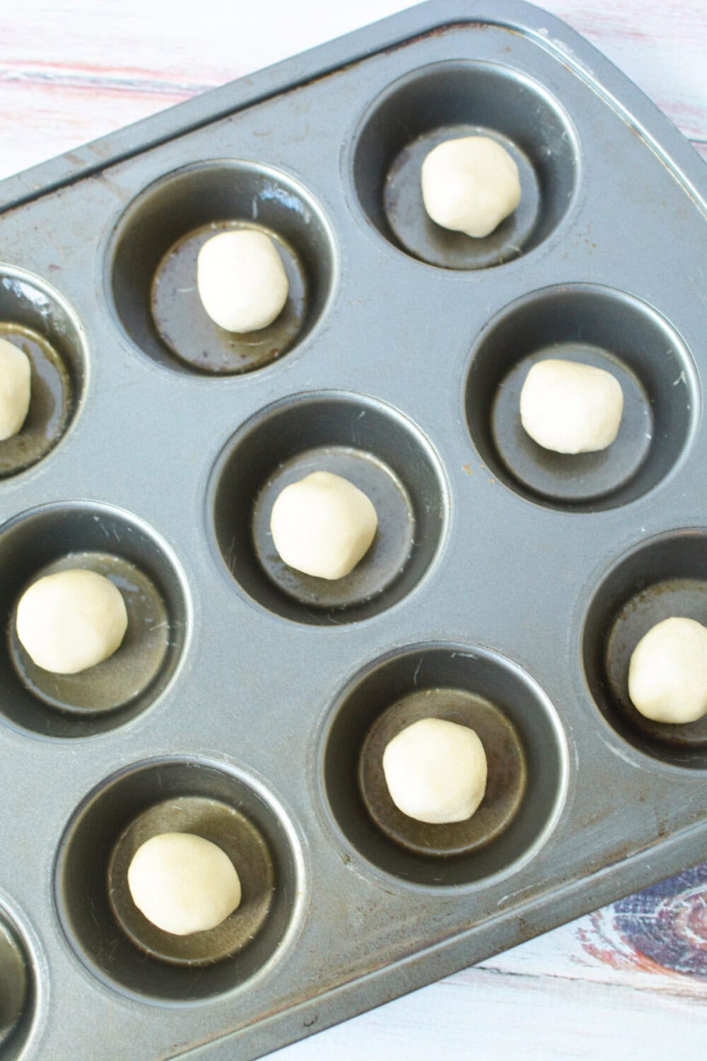 Balls of sugar cookie dough in a muffin tin.