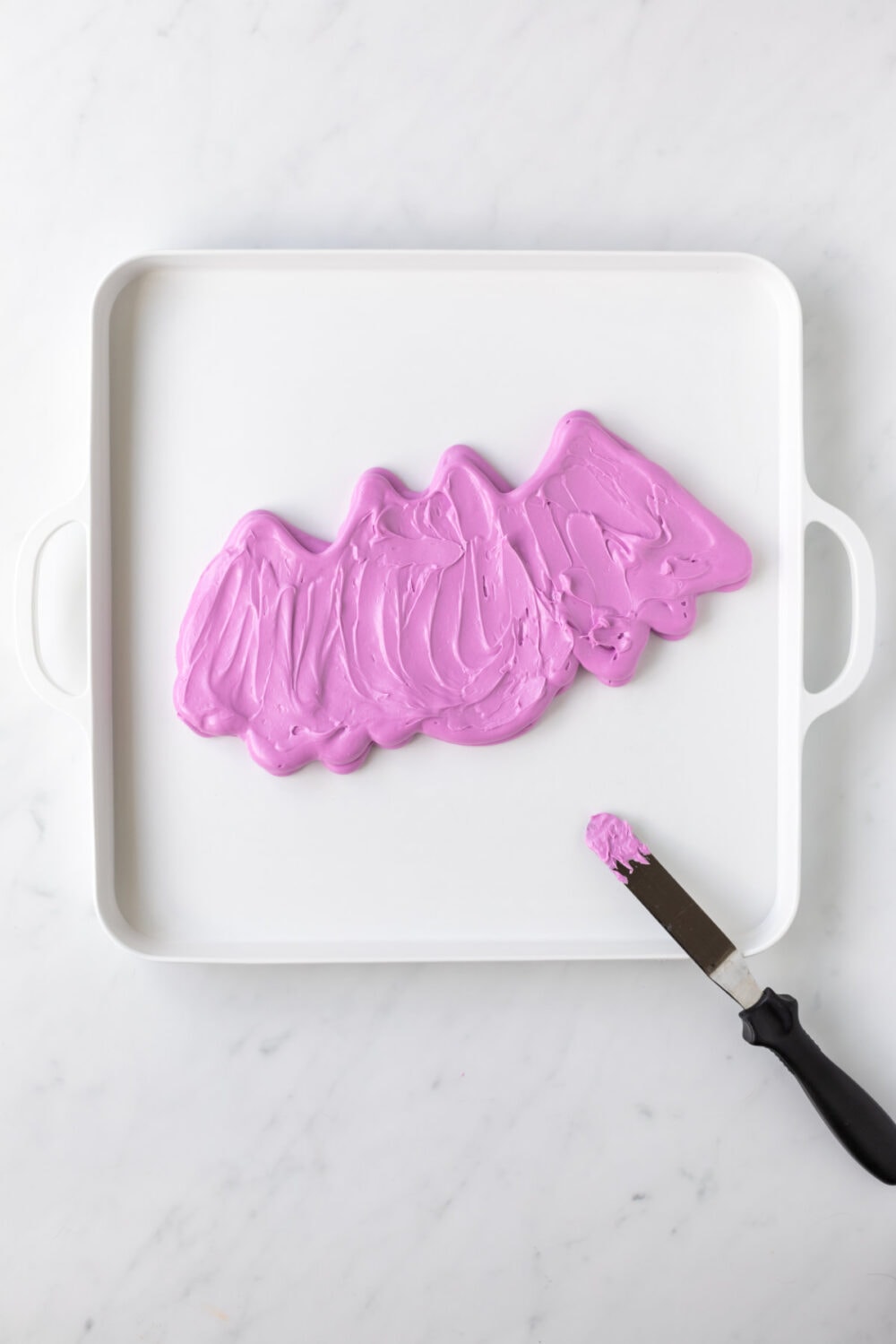 Using an offset spatula to smooth out purple frosting bat. 