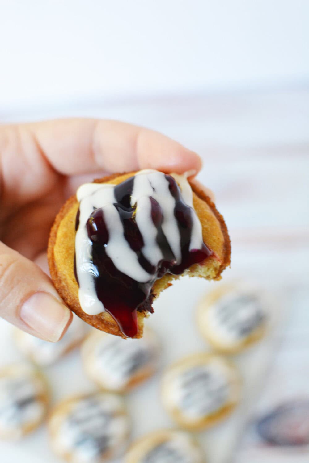 Holding a glazed blueberry pie sugar cookie with a bite missing. 
