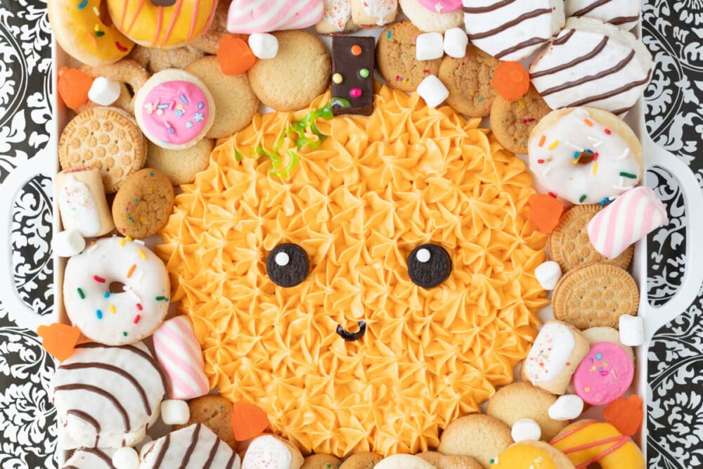 Orange frosting pumpkin on a board surrounded by sweets. 